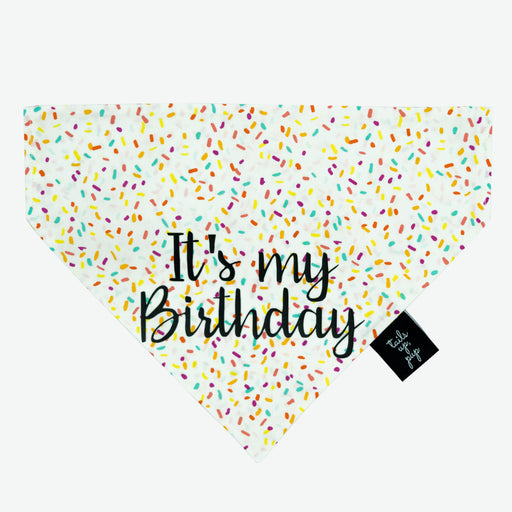 White dog bandana with coloured sprinkles with the words "It's my birthday" on it. The bandana is placed on a white background.
