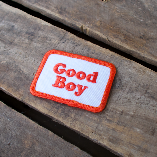 Scouts Honour "Good Boy" iron-on badge with red text and a white background, laid out on a wooden table.