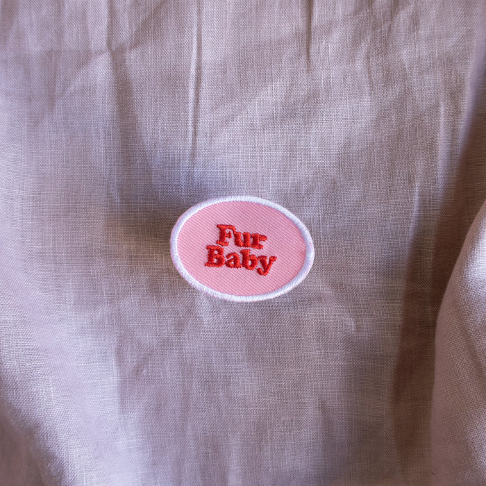 Scouts Honour Fur Baby iron-on badge in pink and red complemented by a white round border laid out on a fabric cloth.