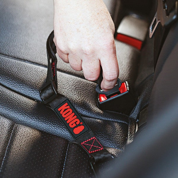 A close-up of a hand fastening a black KONG branded car seat belt buckle onto a black leather car seat.