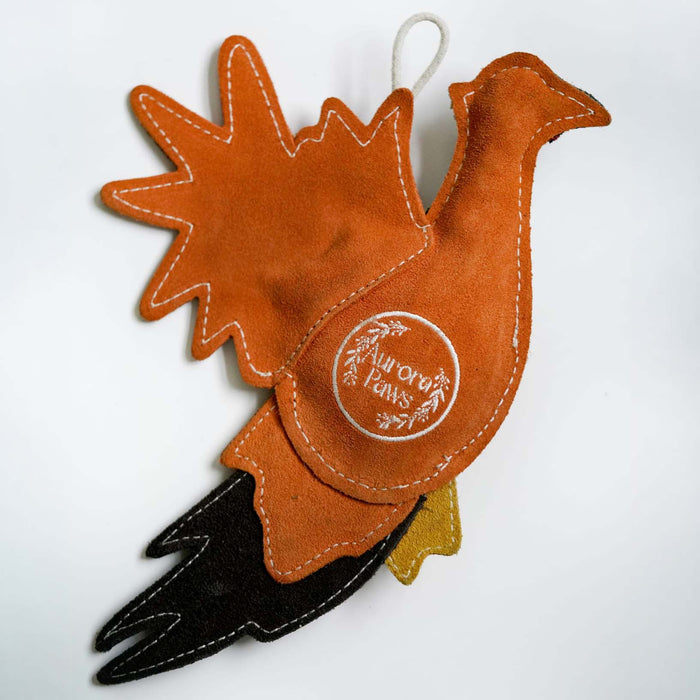A handmade felt Christmas ornament shaped like a turkey, featuring a warm orange-brown body and tail, a black beak, a small mustard yellow wing, and white contrast stitching. A circular white logo patch reading 'the orange farm' is stitched onto the side, and a white hanging loop is attached at the top.