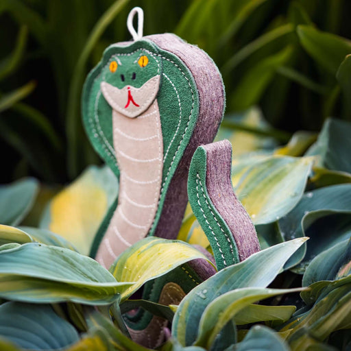 A felt snake garden ornament with a green head and body, a purple tail, and a beige underbelly, nestled among green and yellow hosta leaves.