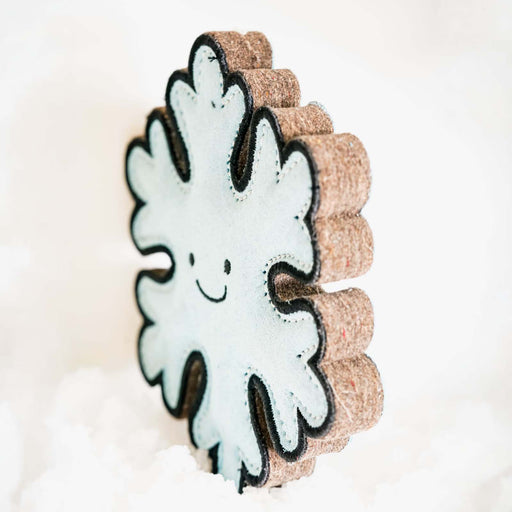 A snowflake-shaped decorative item with a white felt center, black embroidered smiley face, and textured brown cork borders, standing upright against a soft white background.