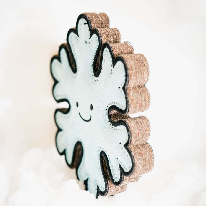 A snowflake-shaped decorative item with a white felt center, black embroidered smiley face, and textured brown cork borders, standing upright against a soft white background.