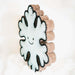 A snowflake-shaped decorative item with a white felt center, black embroidered smiley face, and textured brown cork borders, standing upright against a soft white background.