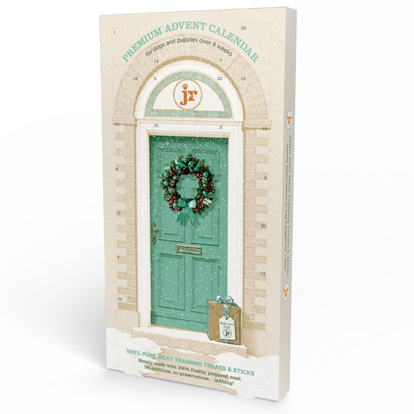 Premium Advent Calendar box featuring an illustration of a teal holiday door with a wreath, on a cream brick-patterned background. The front shows the text 'PREMIUM ADVENT CALENDAR for cats and puppies over 4 weeks' and a small gift bag with a letter.