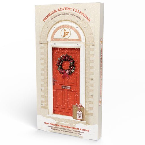 A boxed advent calendar package standing upright on a white studio background. The front shows an illustrated red front door with a holiday wreath, arched doorway details, and red text reading 'PREMIUM ADVENT CALENDAR' and 'for dogs and puppies over 4 weeks.