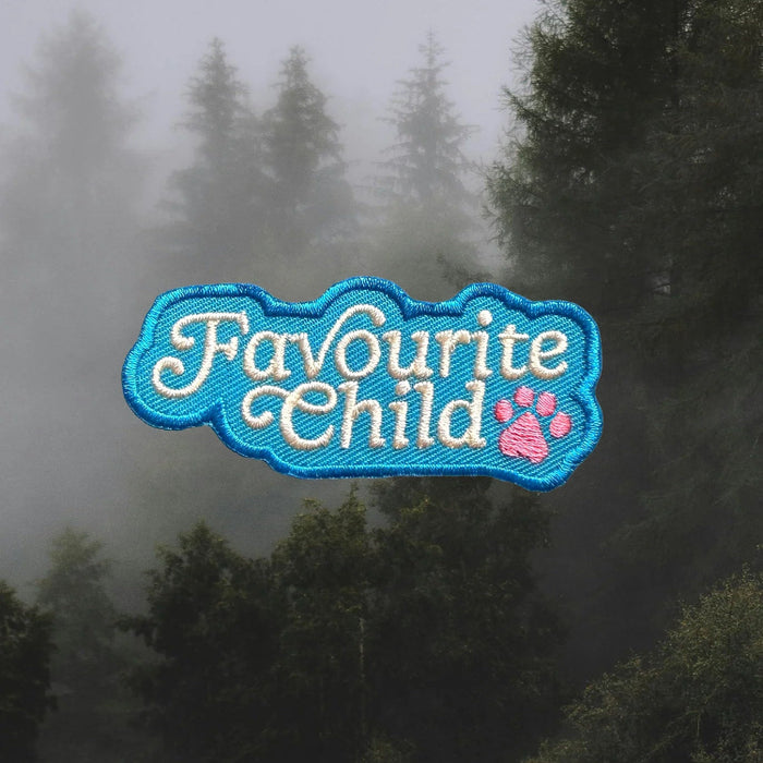 Embroidered patch with 'Favourite Child' text and paw print on a foggy forest background