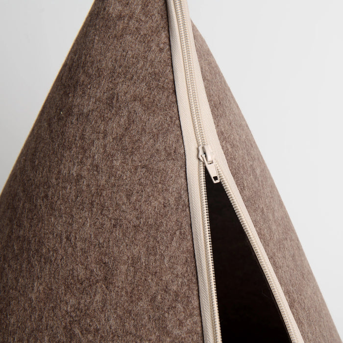 Close-up of a brown felt cone tent with a cream-colored zipper and a dark interior, set against a light gray background.