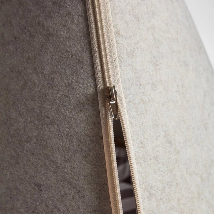 Close-up of a beige zipper running vertically down the center of a light gray fabric-covered cylindrical object, with a small metallic zipper pull visible.