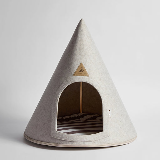 A cone-shaped pet house made of light gray felt, featuring a triangular metal brand plaque on the front and a striped cushion inside, photographed on a neutral light gray background.