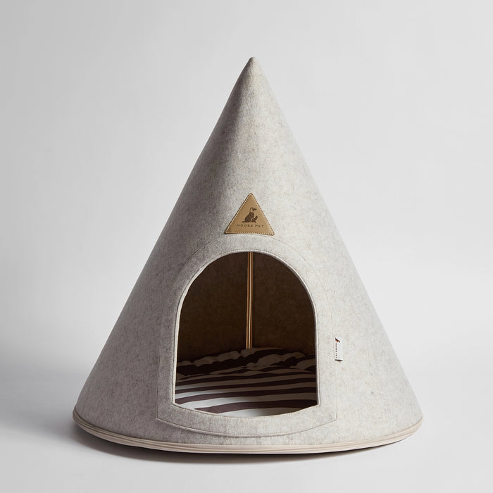 A cone-shaped pet house made of light gray felt, featuring a triangular metal brand plaque on the front and a striped cushion inside, photographed on a neutral light gray background.