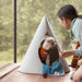 Person interacting with a small dog inside a cone-shaped pet bed by a window.