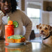 Woman and dog looking at a Bloody Mary and sandwich on a table.
