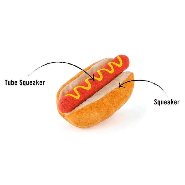 A plush hot dog toy with a red sausage, yellow mustard, and beige bun on a white background, with text labels pointing to the 'Tube Squeaker' and 'Squeaker' areas.