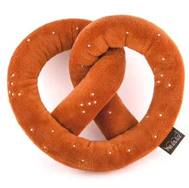 A plush pretzel-shaped pillow in a warm brownish-orange color, decorated with small white faux-seed details and a small black brand tag on the right side, shown on a plain white background.