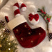 A red velvet Christmas stocking with gold star embroidery, a white faux-fur cuff, and a candy cane-shaped pull, styled on a white faux-fur surface with pinecones, evergreen branches, and a small white ornament with a red bow.