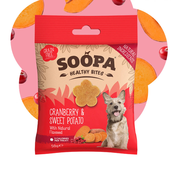 A package of Soopa Healthy Bites Cranberry & Sweet Potato dog treats, featuring a red and beige bag with a picture of a dog and illustrations of treats, set against a pink background with orange and red circular accents.
