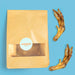 A paper bag with a clear window and a round white label reading 'WOOOF' sits on a bright blue background, alongside two dried chicken feet.