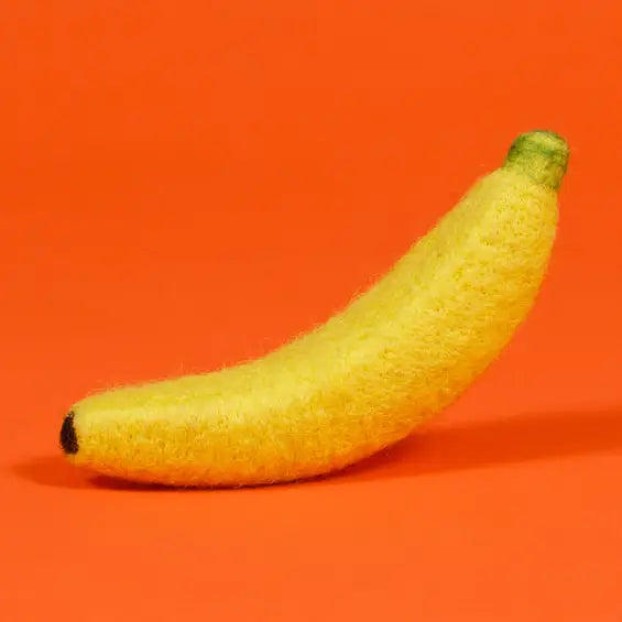 A yellow felt banana with a green stem and dark tip, set against a solid orange background.