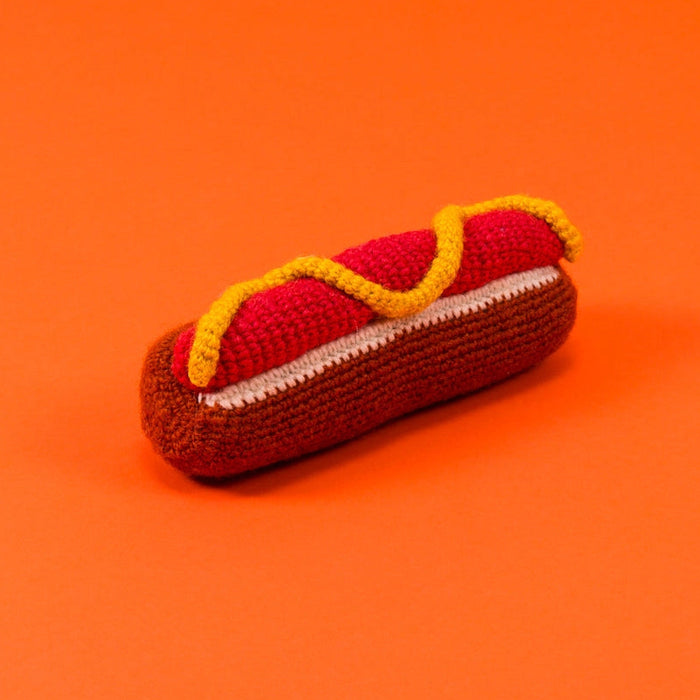 Knitted hot dog toy with a bun on an orange background
