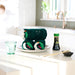 Modern kitchen with a table set for sushi, featuring a bottle of wasabi and a glass of water.