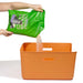 Green bag of dog food being poured into an orange storage bin on a white background