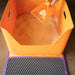 Orange cat litter box with purple base and a scoop adding litter inside.
