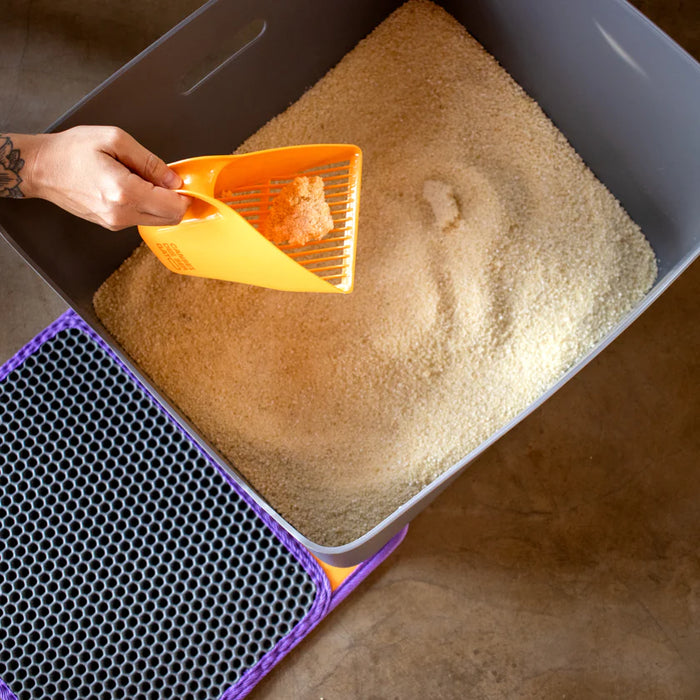 Person using a yellow scoop to clean a cat litter box with brown litter.