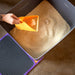 Person using a yellow scoop to clean a cat litter box with brown litter.