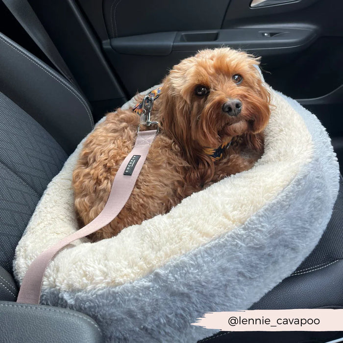 Dog sitting in a car seat cover with a visible brand logo.