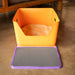 Orange litter box with a purple mat on a wooden floor