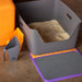 Cat litter box set with orange container, gray scoop, and purple mat on a brown surface.