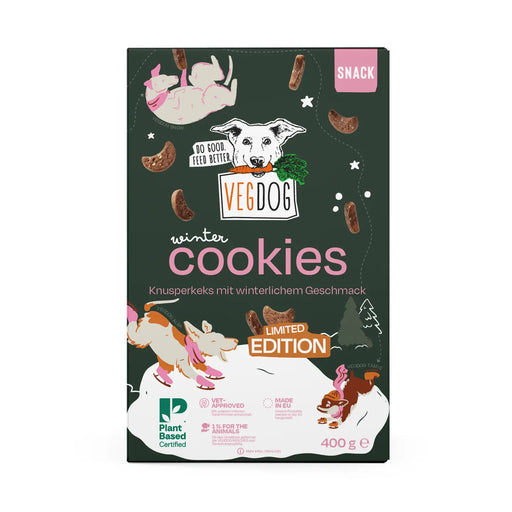 VegDog Winter Cookies Limited Edition dog snack packaging, featuring a dark forest green background with pink and white illustrations of a dog, a cat, and a squirrel, and brown cookie pieces scattered around.