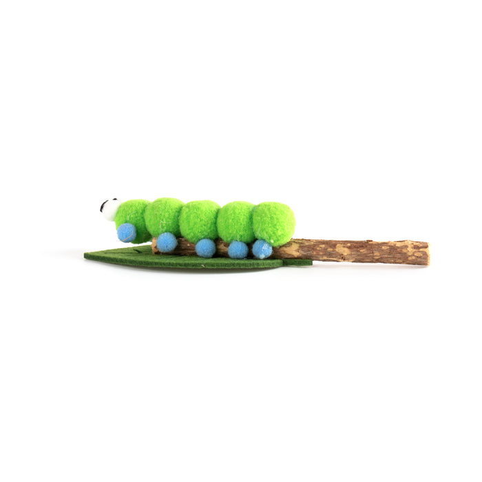 A green caterpillar-themed hair claw clip featuring bright green fuzzy segments, small blue bead details, a green leaf base, and a brown twig tail on a plain white background.