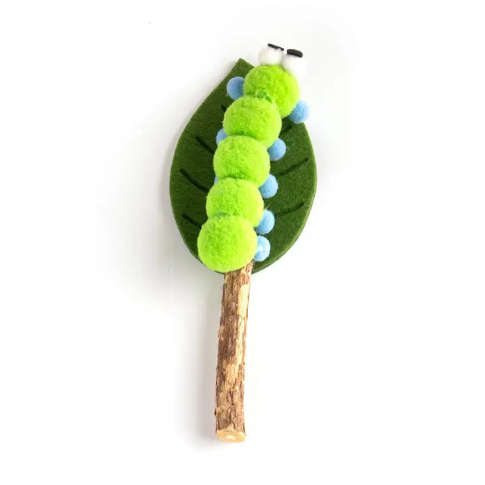 A handmade felt caterpillar and leaf craft on a twig, featuring bright green fuzzy caterpillar bodies, light blue felt accents, a dark green felt leaf, and a natural brown twig tail, set against a plain white background.