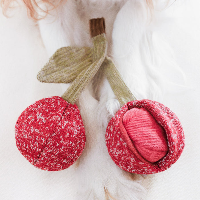 Red knitted cherry-shaped toy with green stems on a white background