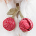Red knitted cherry-shaped toy with green stems on a white background