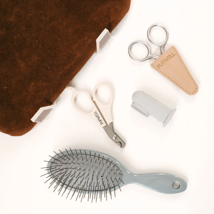A grooming kit laid out on a white background, including a brown velvet brush or cushion, silver nail clippers with a tan leather pouch labeled 'NURWELL', white-handled shears labeled 'TENMAI', a gray comb, and a gray hairbrush.