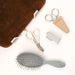 A grooming kit laid out on a white background, including a brown velvet brush or cushion, silver nail clippers with a tan leather pouch labeled 'NURWELL', white-handled shears labeled 'TENMAI', a gray comb, and a gray hairbrush.
