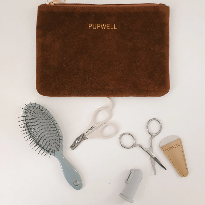 A brown suede grooming pouch with gold 'PUPWELL' lettering, displayed with grooming tools on a white background: a gray brush, white-handled scissors, silver nail scissors, a beige leather sleeve, and a gray nail file.