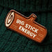 An embroidered patch shaped like a log with the words 'BIG STICK ENERGY' in white, placed on a dark green knit fabric background.