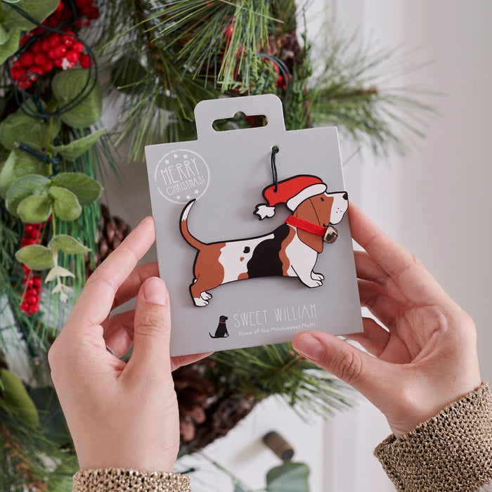 A basset hound Christmas ornament held by human hand from a snowy tree branch