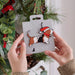 A basset hound Christmas ornament held by human hand from a snowy tree branch