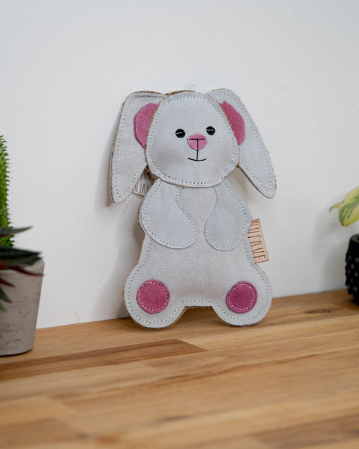 NufNuf Suede Bunny dog toy in White with pink accents and a leather NufNuf label on a wooden table.