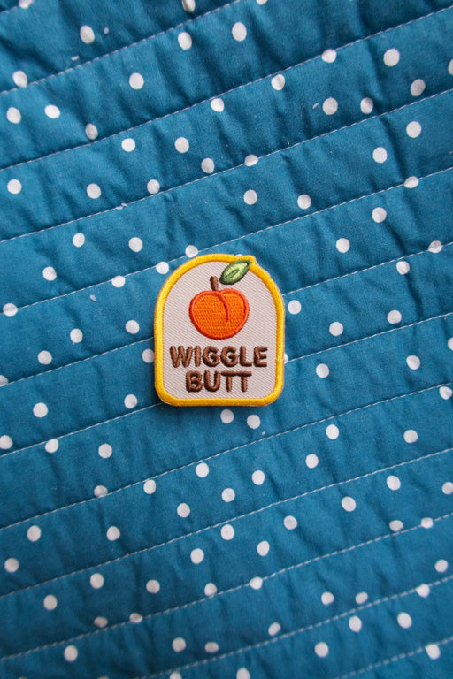 Scouts Honour "Wiggle But" iron-on badge with orange peach icon, laid out on a blue and white polkadot backdrop