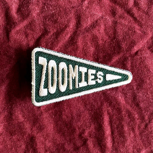 Scouts Honour "Zoomies" pennant-shaped iron-on badge in green and white on a linen burgundy backdrop