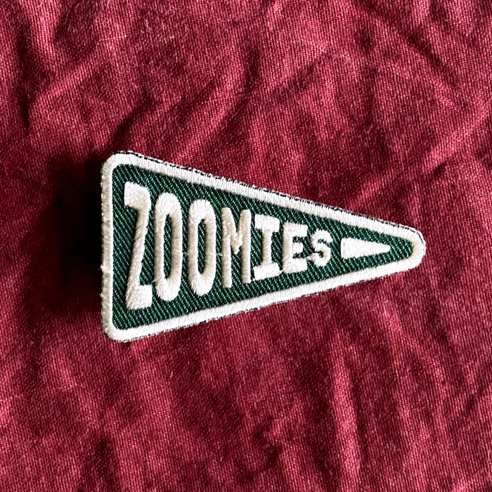 Scouts Honour "Zoomies" pennant-shaped iron-on badge in green and white on a linen burgundy backdrop