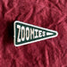 Scouts Honour "Zoomies" pennant-shaped iron-on badge in green and white on a linen burgundy backdrop