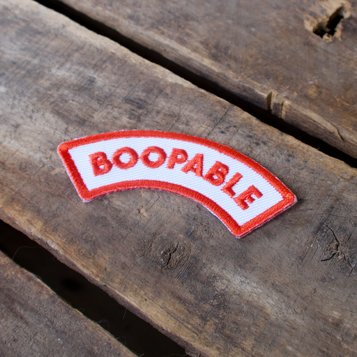 Scouts Honour Boopable iron-on badge in maroon and white laid out on a wooden table.